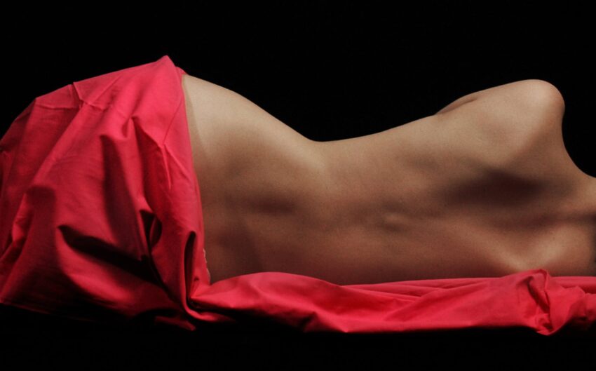 Elegant nude art photo of a woman draped in red fabric on a black background.